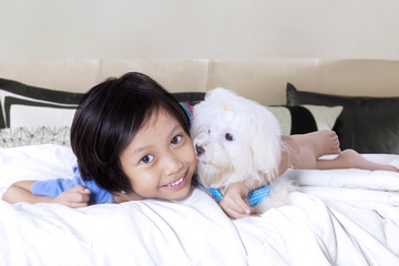 Cheerful girl hugs maltese dog on bed