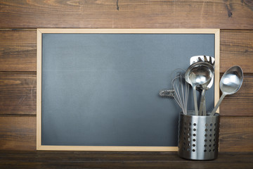 Pizarra vacía con espacio para texto sobre fondo de madera y utensilios de cocina
