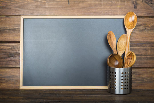 Pizarra vac&iacute;a con espacio para texto sobre fondo de madera y utensilios de cocina