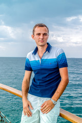 Young Sailor relaxing happily on the vacation sailboat yacht standing on a deck having a rest on summer boat over blue ocean wave splashes background