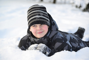 Fototapeta na wymiar Teen boy lies on snow in the winter forest