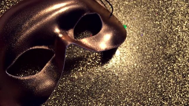 Colorful confetti falling and bouncing off golden carnival mask sitting on sparkly textured gold background
