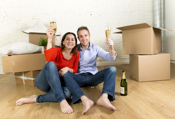 Fototapeta na wymiar happy American couple sitting on floor unpacking together celebrating with champagne toast moving in a new house