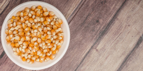 Raw popcorn in white bowl over wooden background