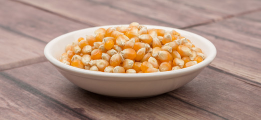 Raw popcorn in white bowl over wooden background