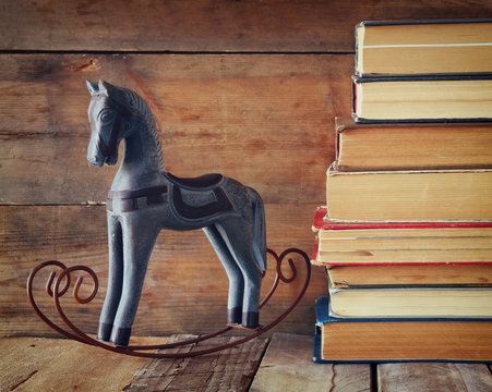 stack of old books next to decorative rocking horse wooden table. vintage filtered image
