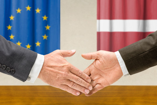 Vertreter der EU und Lettlands reichen sich die Hand
