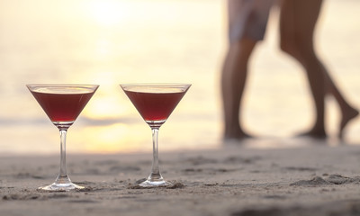 Two cocktails on the beach with couple kissing in background