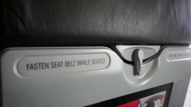 Fasten seat belt while seated and life vest under the seat sign across airplane seating. Abstract safety