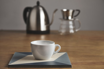 White coffee cup in front of teapot and drip coffee maker
