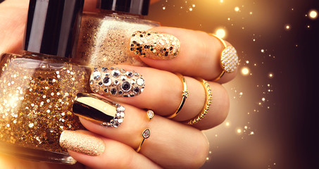 Goldene Maniküre mit Edelsteinen und Funkeln. Flasche Nagellack, trendige Accessoires