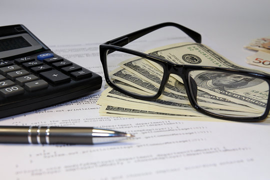 Glasses, calculator, bancnote and pen on desk