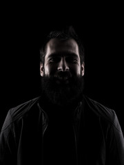 Desaturated laughing man looking at camera. High contrast low key dark shadow portrait isolated over black background.