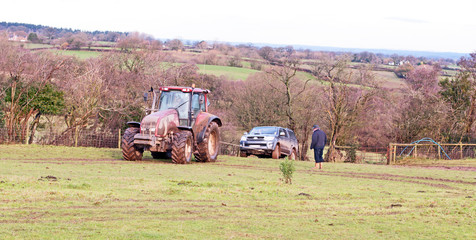 Tractor towing a vehicle from a muddy field in the winter