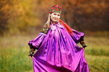 Beautiful pretty girl in national bright purple dress with red kerchief on her head, ornaments and embroidery. Colorful bokeh autumn nature, yellow leaves. Candid portrait, vivid colors.