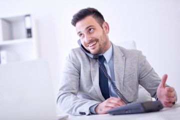 Naklejka premium Businessman on phone while using laptop in the office