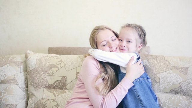Little girl kisses mother cheek, closeup view at sofa