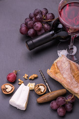 Red wine bottle, grapes, walnuts and cheese on a wooden background