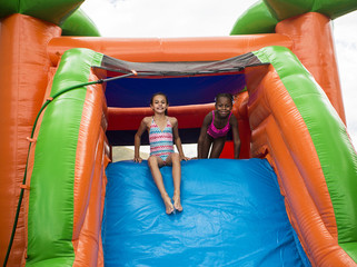 Fototapeta na wymiar Happy little girls sliding down an inflatable bounce house