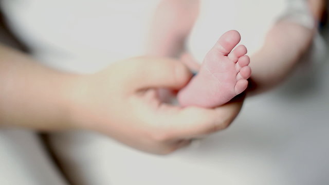 Newly made mother shows little foot of her newborn baby. Mom tickles child's heel. Cozy tender family morning at home. 