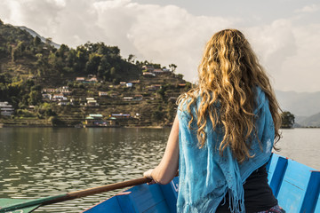 Woman paddling boat toward village on hill.