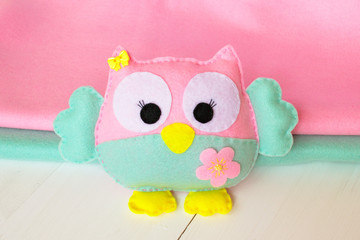 Felt owl on a white wooden background, rolls of pink and blue felt 