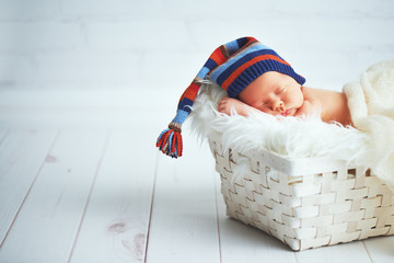 Cute newborn baby in blue knit cap sleeping in basket