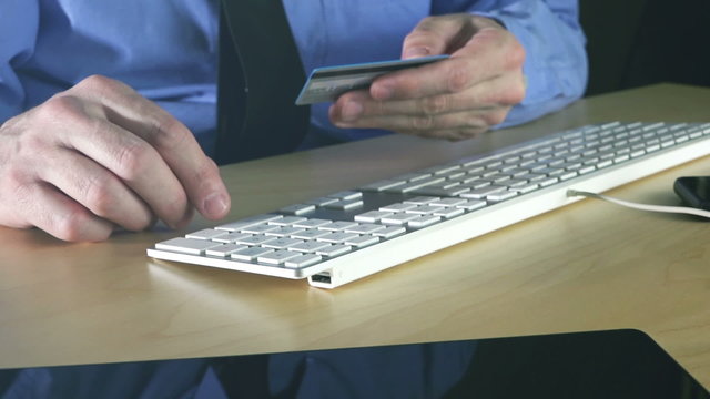 Businessman using credit card for online transaction with office desktop computer.