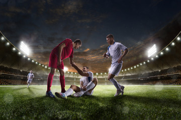 Soccer player helps onother one on sunset stadium background panorama - obrazy, fototapety, plakaty