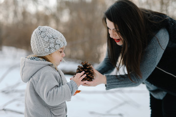Pregnant Mother playing with her baby girl on winter cold sunset in park, smiling and enjoy good times