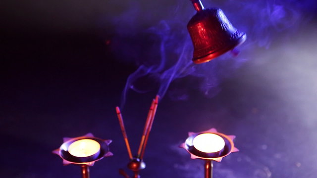 Sound vibrations - Buddhist Temple Bells. Hand holding bell
 on  blue background with red light filter and incense. Asian spiritual traditions, ritual musical instruments.  Puja. Mystical atmosphere