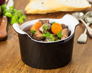 Boeuf bourguignon in black  pot on a  wooden  table. Selective focus.