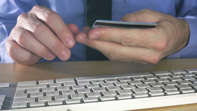 Businessman using credit card for online transaction with office desktop computer.