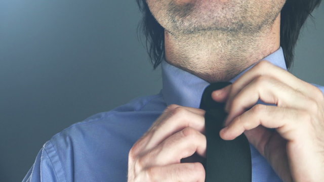 Cool young adult businessman adjusting his necktie in office before important business meeting or interview