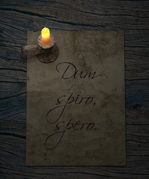 Dum spiro spero latin proverb. While I brethe, I hope. Old paper and candle on rustic wooden table.