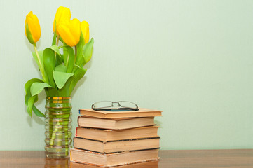 Old books with a bouquet of tulips on a wooden table