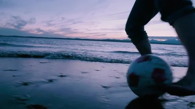 Man  Dribbling  Soccer  Ball  in  Front  of  Waves  at  Sunset