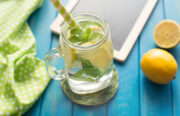 Lemonade with lemon slices and mint in a jar mug with straw on blue wooden background from top view. Water with lemon. Detox.