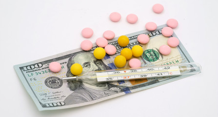 Thermometer, pills and vitamins on a hundred dollar bill