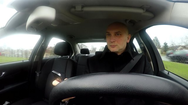 Young man texting and looking at his smartphone while driving a car, putting other drivers in harm's way and jeopardy with his style of reckless and irresponsible driving. View from windscreen.