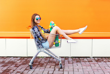 Fashion smiling cool girl having fun sitting in shopping trolley