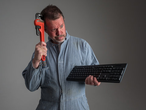 Humorous photo of repairman scratching his head with a pipe wrench as he stares at computer keyboard, suggesting the wrong tool for the job.