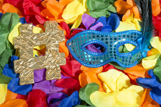 Sparkly blue carnival mask sits next to golden hashtag on bright background of rainbow colored flower leis in a celebratory pile