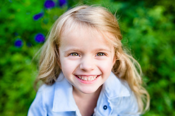 Close-up portrait of a smiling blond little girl wearing a blue jacket in sunny summer day