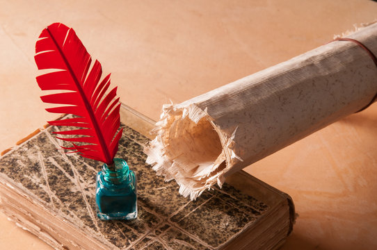 Red quill pen and a rolled papyrus sheet on an old book