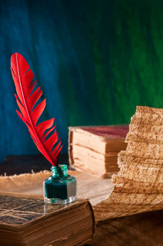 Red quill pen and a papyrus sheet and old books in a blue and green background