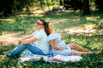 pregnant wife and her husband sitting outdoors on the grass
