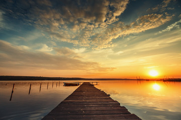 Boat and jetty on lake with a reflection in the water at sunset