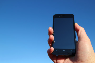 black smart phone and the hand in the blue sky