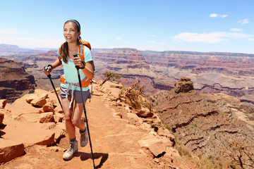 Smiling young female hiker walking on Grand Canyon. Full length of beautiful woman holding hiking poles while climbing rocky mountains. Attractive trekker is enjoying vacation. © Maridav